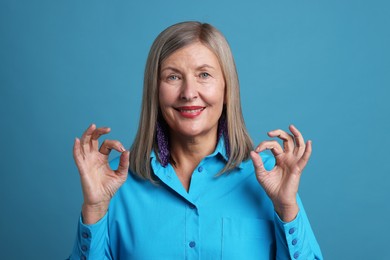 Senior woman showing okay gesture on blue background