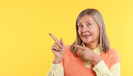 Photo of Senior woman pointing at something on yellow background