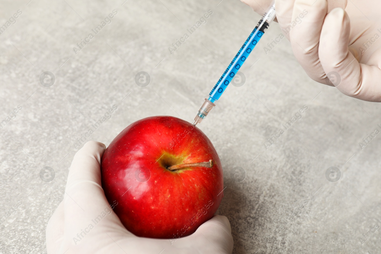 Photo of GMO concept. Scientist injecting something into fresh apple at grey table, closeup