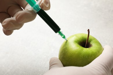 Photo of GMO concept. Scientist injecting something into green apple at grey table, closeup