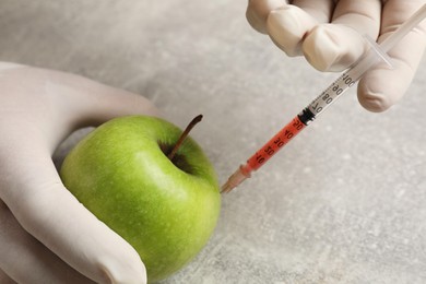 Photo of GMO concept. Scientist injecting something into green apple at grey table, closeup