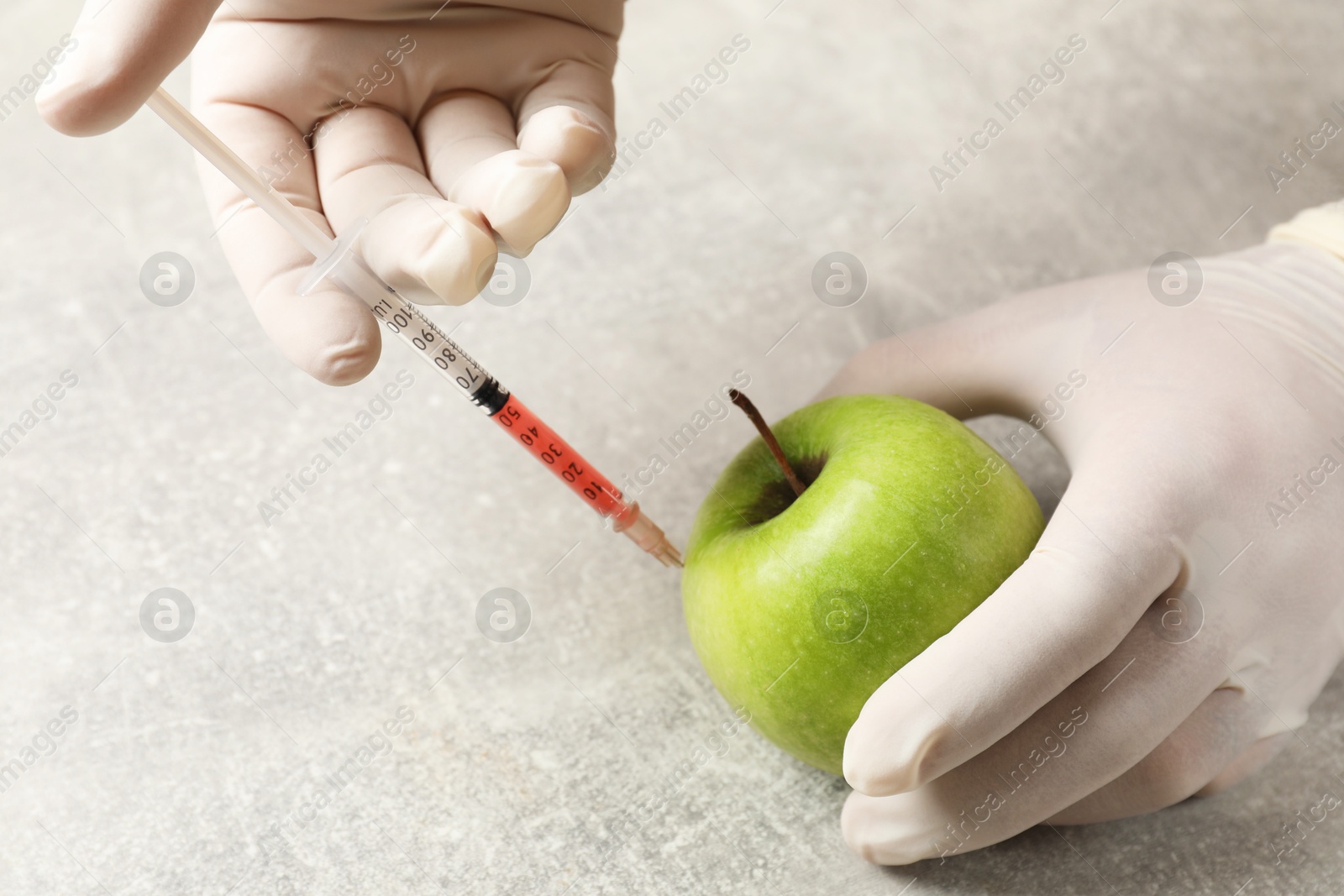 Photo of GMO concept. Scientist injecting something into green apple at grey table, closeup