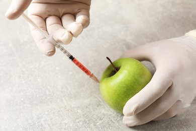 Photo of GMO concept. Scientist injecting something into green apple at grey table, closeup