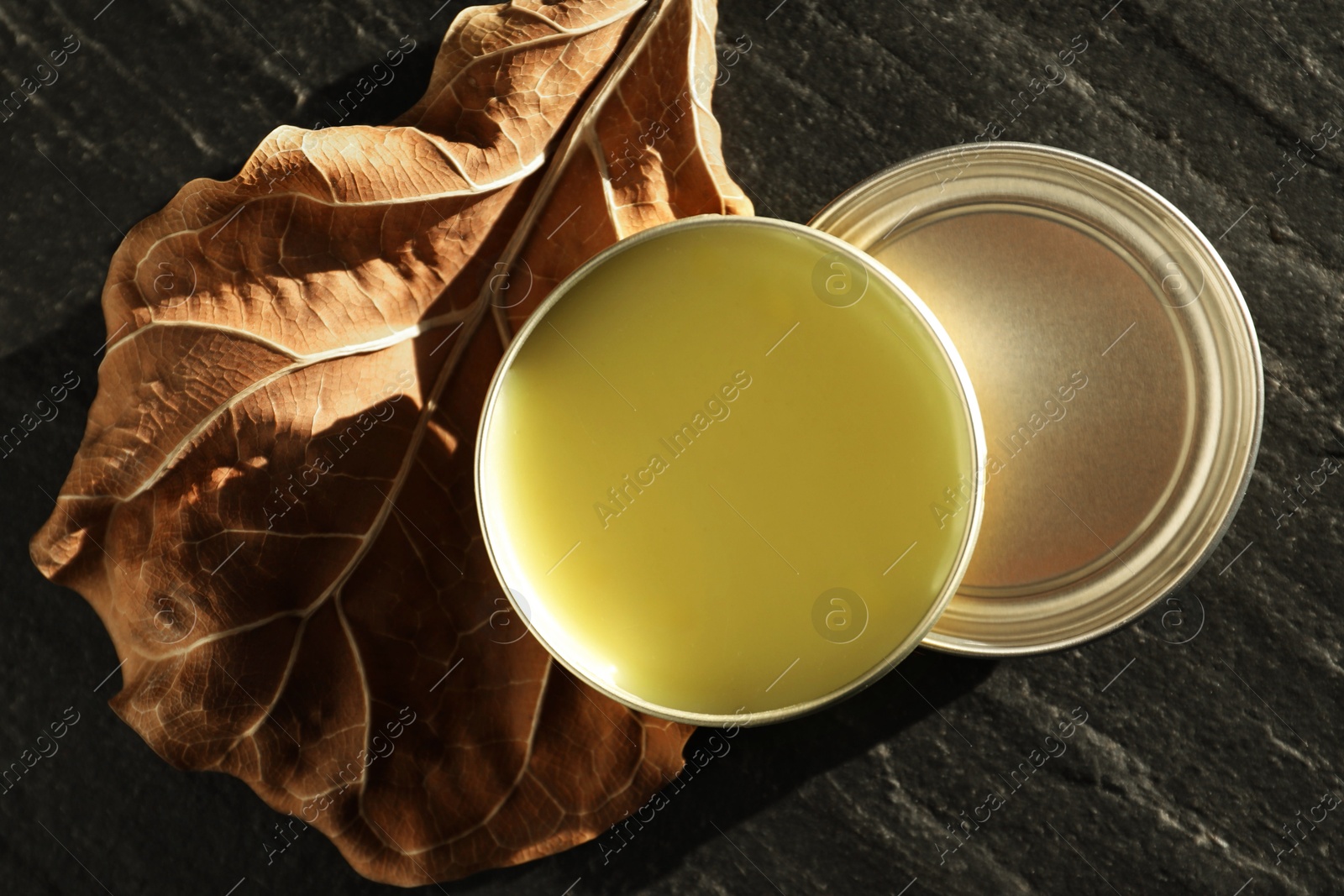 Photo of Natural solid perfume and dry leaf on black table, top view