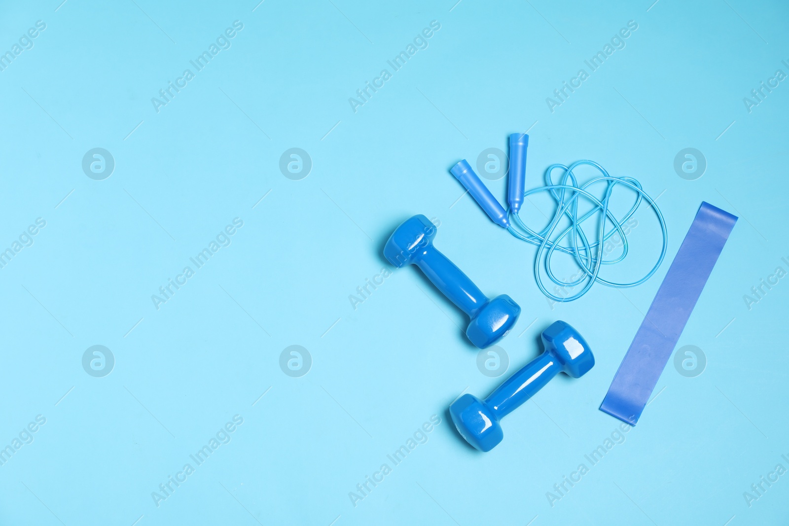 Photo of Sports equipment. Dumbbells, skipping rope and elastic band on light blue background, flat lay. Space for text