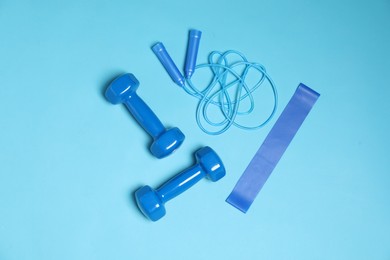 Photo of Dumbbells, skipping rope and elastic band on light blue background, flat lay. Sports equipment