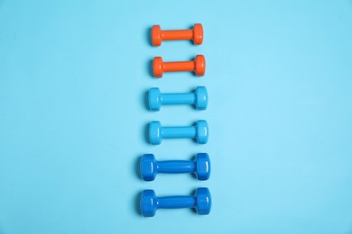 Photo of Different dumbbells on light blue background, flat lay