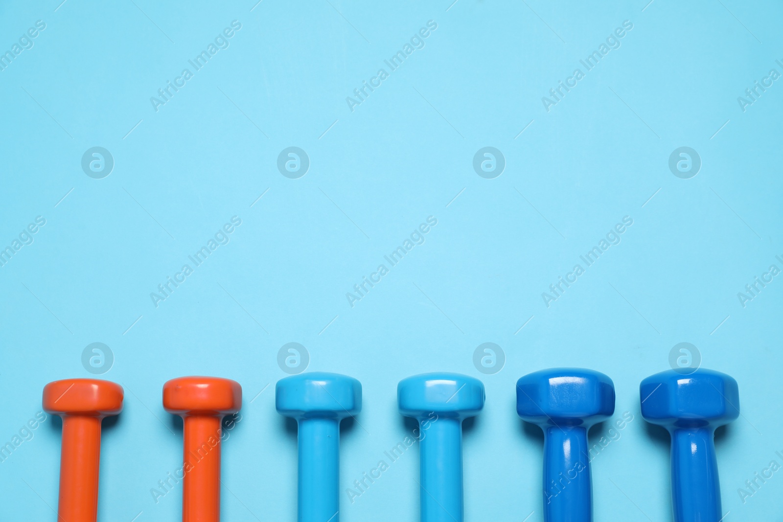 Photo of Different dumbbells on light blue background, flat lay. Space for text