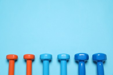 Photo of Different dumbbells on light blue background, flat lay. Space for text