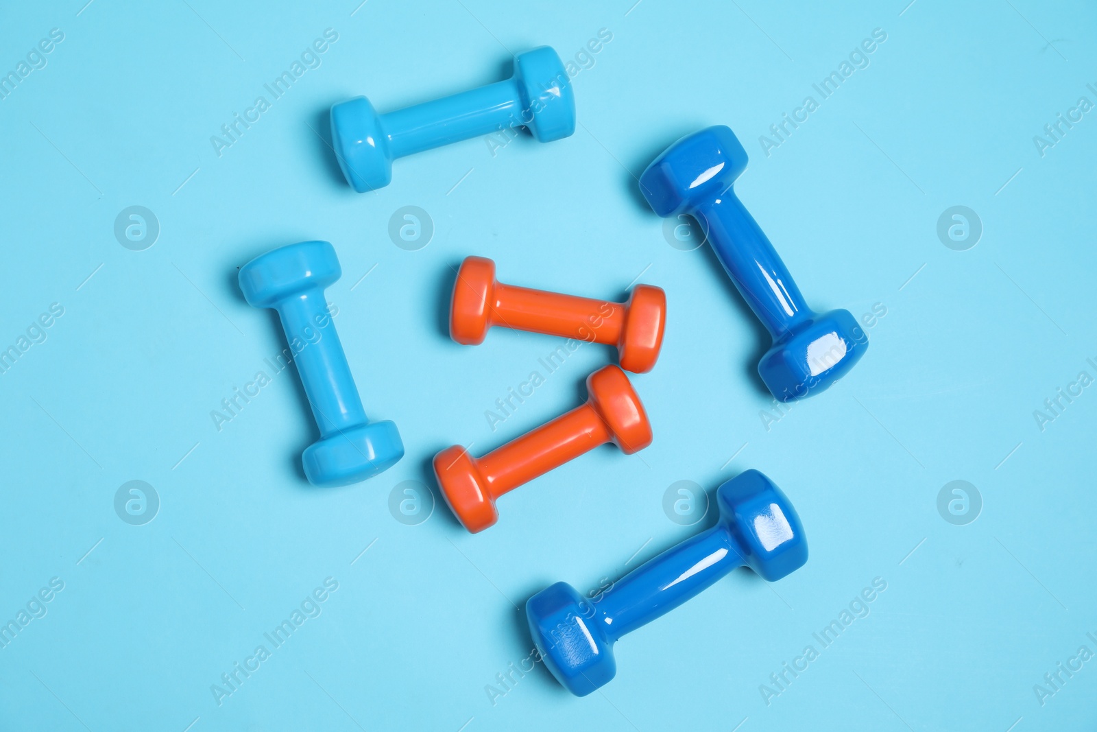 Photo of Different dumbbells on light blue background, flat lay