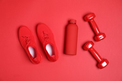 Photo of Dumbbells, water bottle and sneakers on red background, flat lay. Sports equipment