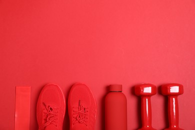 Photo of Sports equipment. Elastic band, water bottle, dumbbells and sneakers on red background, flat lay. Space for text