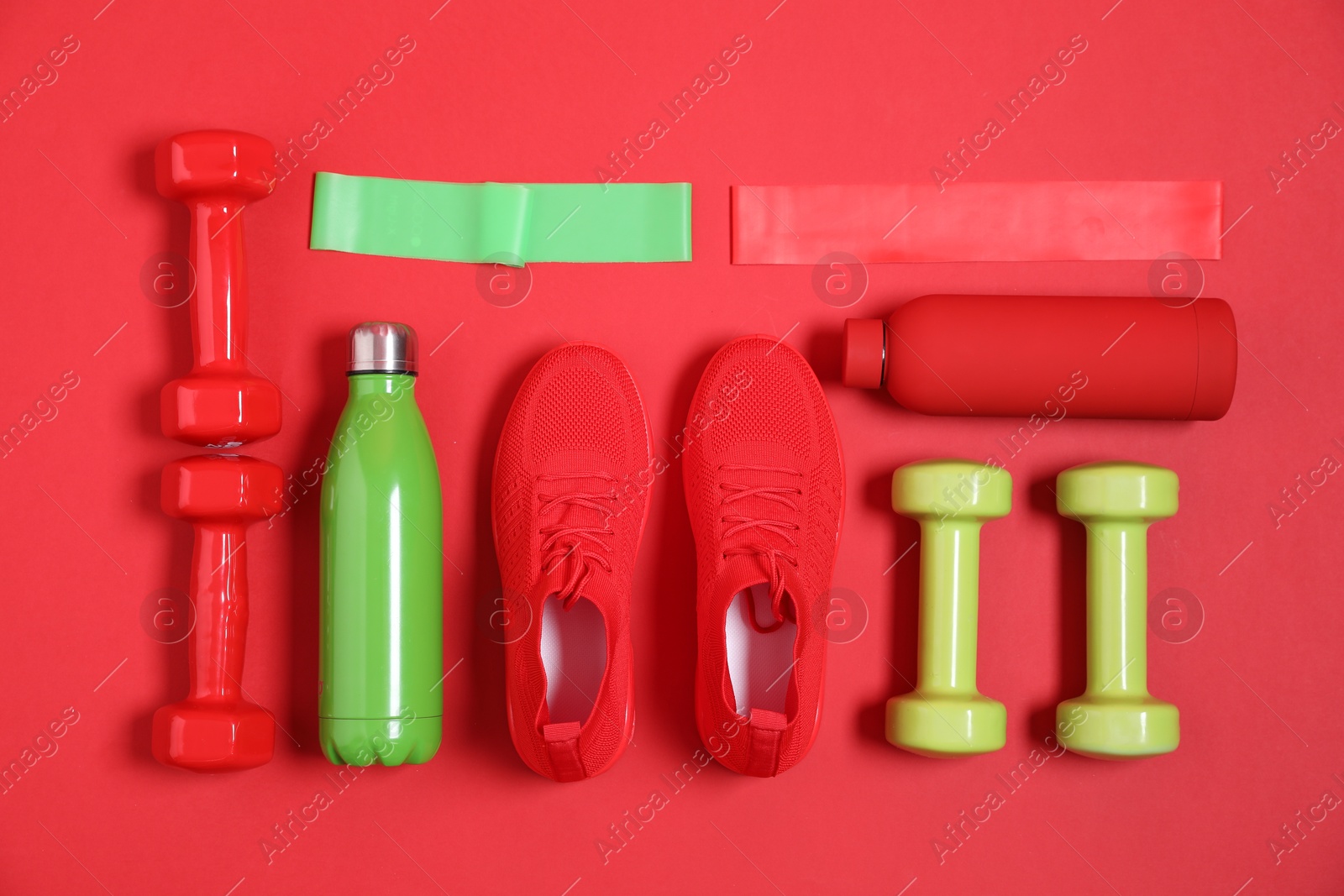 Photo of Elastic bands, water bottles, dumbbells and sneakers on red background, flat lay. Sports equipment