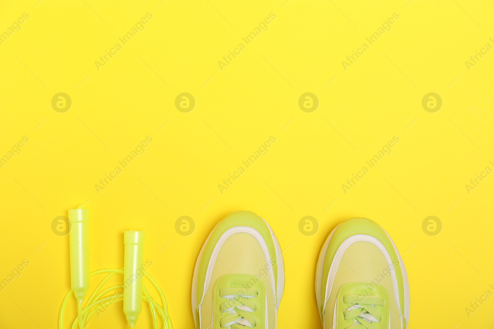 Photo of Sports equipment. Skipping rope and sneakers on yellow background, flat lay. Space for text