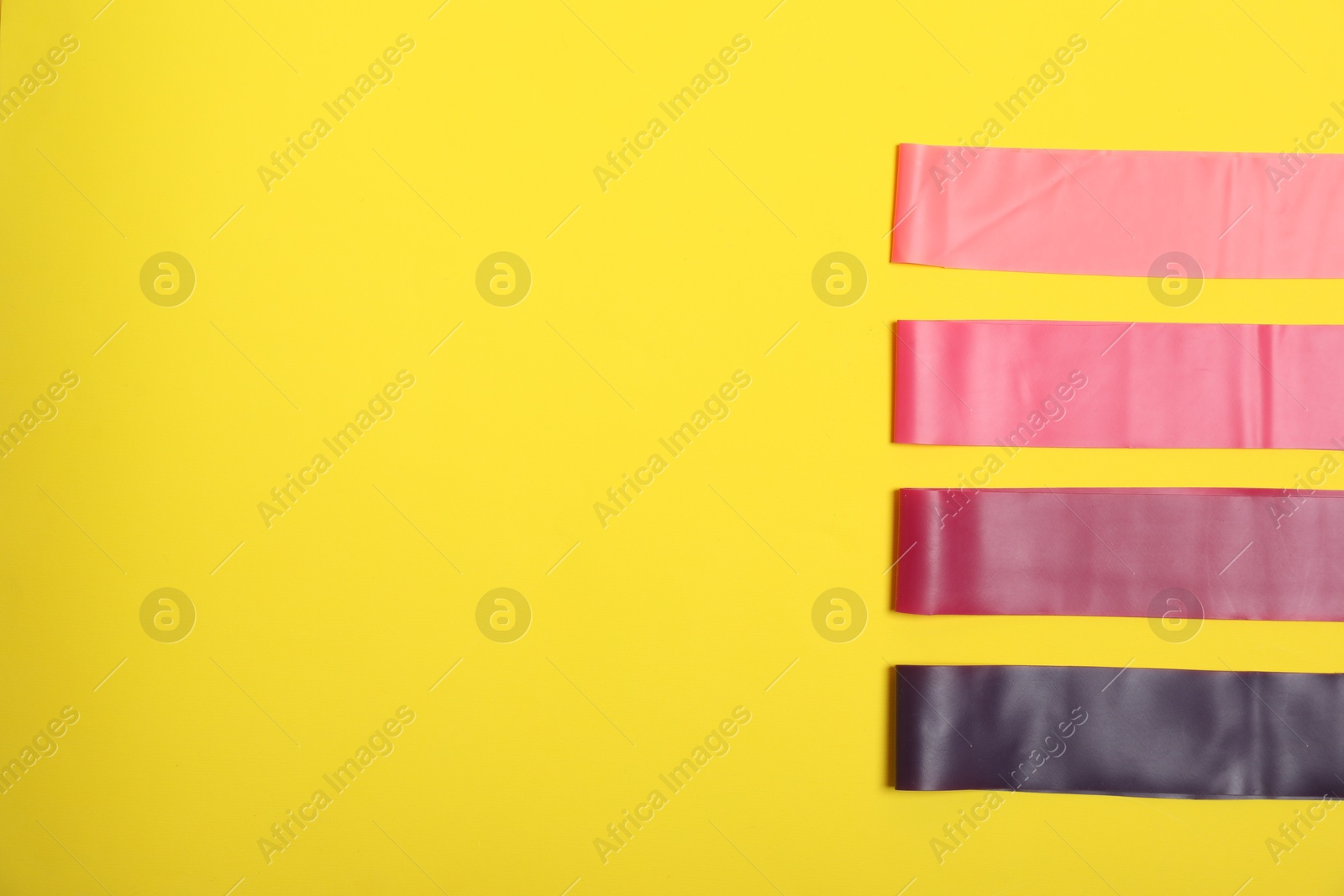 Photo of Sports equipment. Different elastic bands on yellow background, flat lay. Space for text