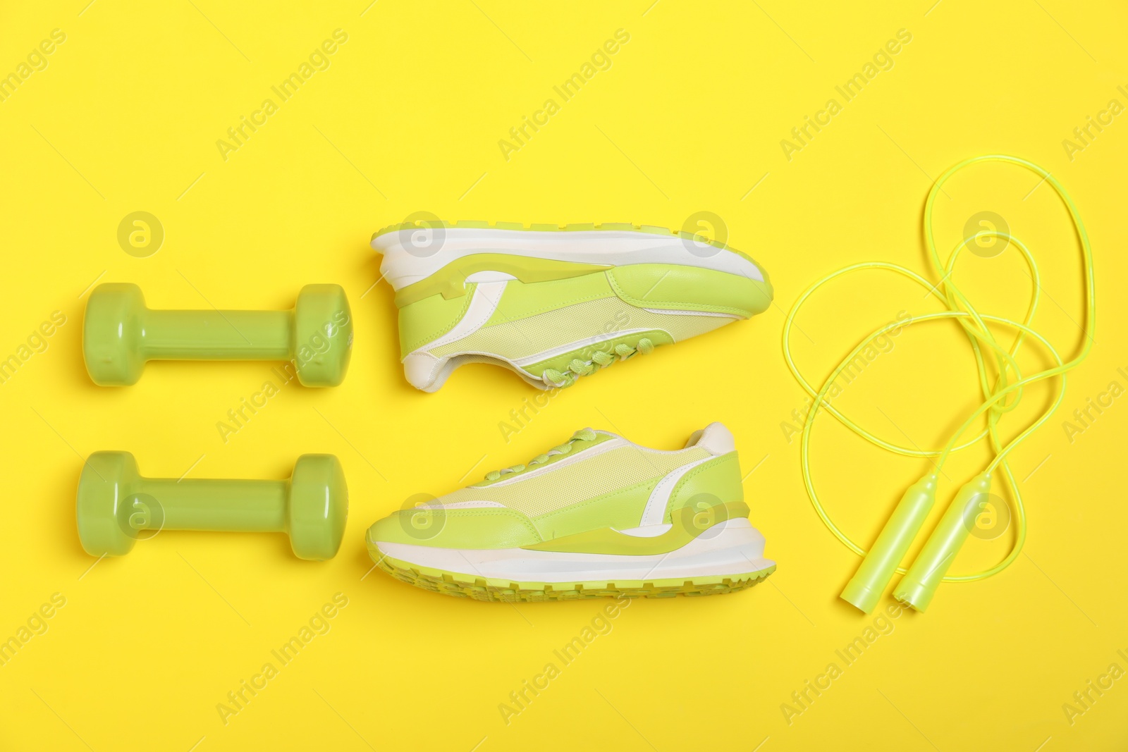 Photo of Dumbbells, skipping rope and sneakers on yellow background, flat lay. Sports equipment