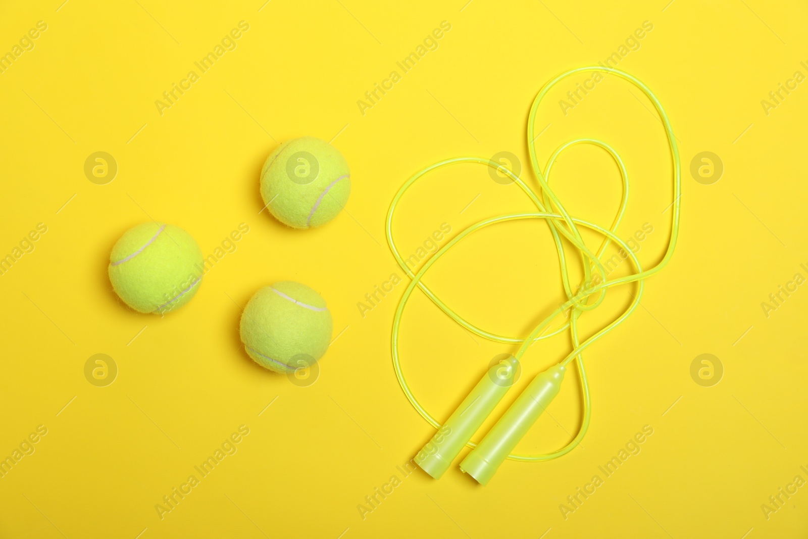 Photo of Skipping rope and tennis balls on yellow background, flat lay. Sports equipment