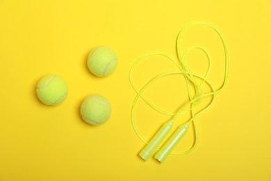 Photo of Skipping rope and tennis balls on yellow background, flat lay. Sports equipment