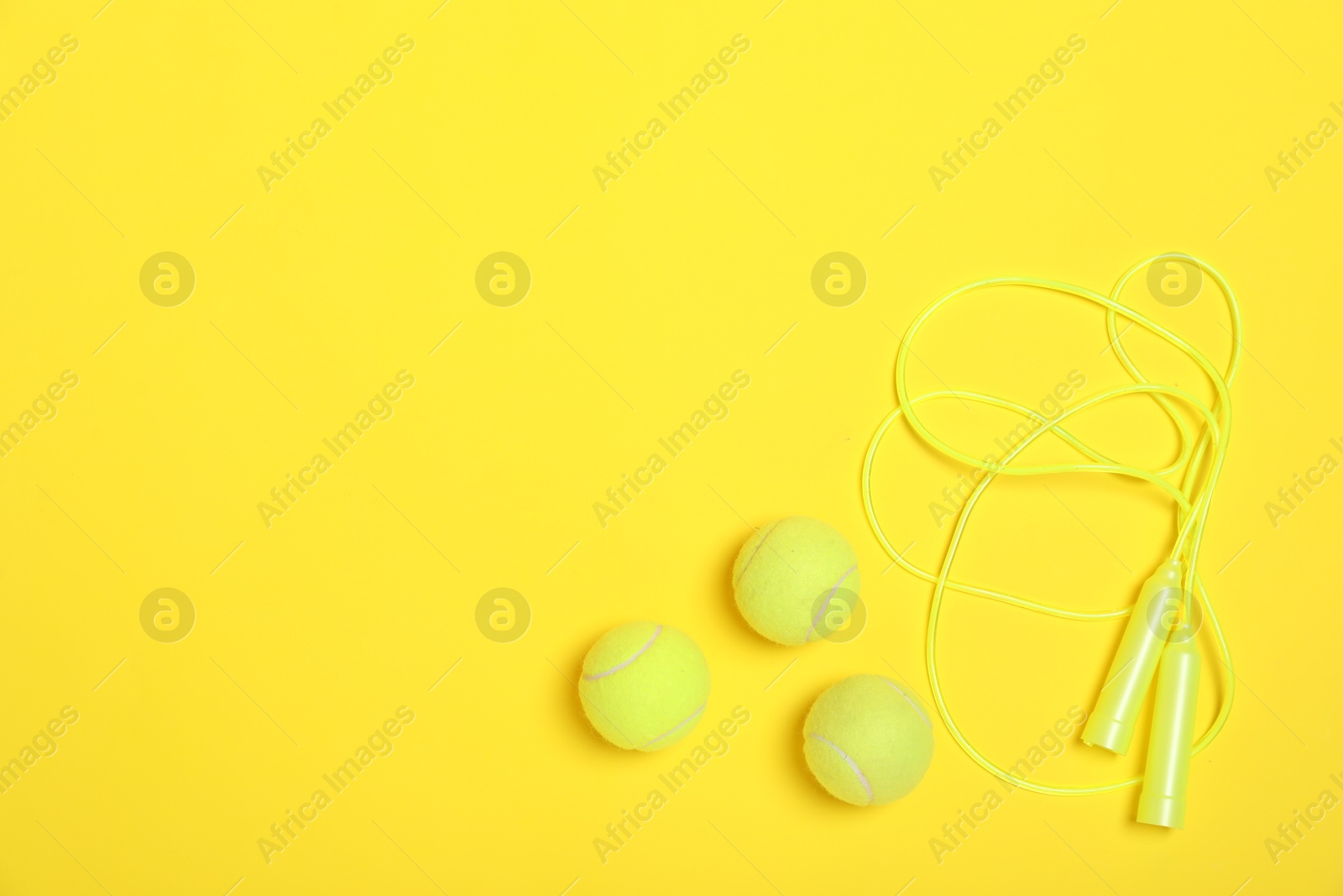 Photo of Sports equipment. Skipping rope and tennis balls on yellow background, flat lay. Space for text