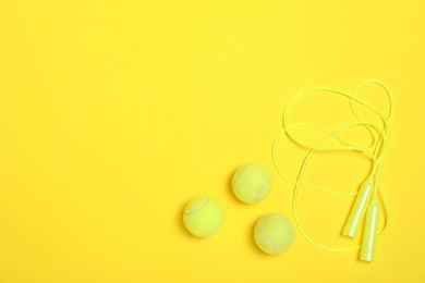 Photo of Sports equipment. Skipping rope and tennis balls on yellow background, flat lay. Space for text