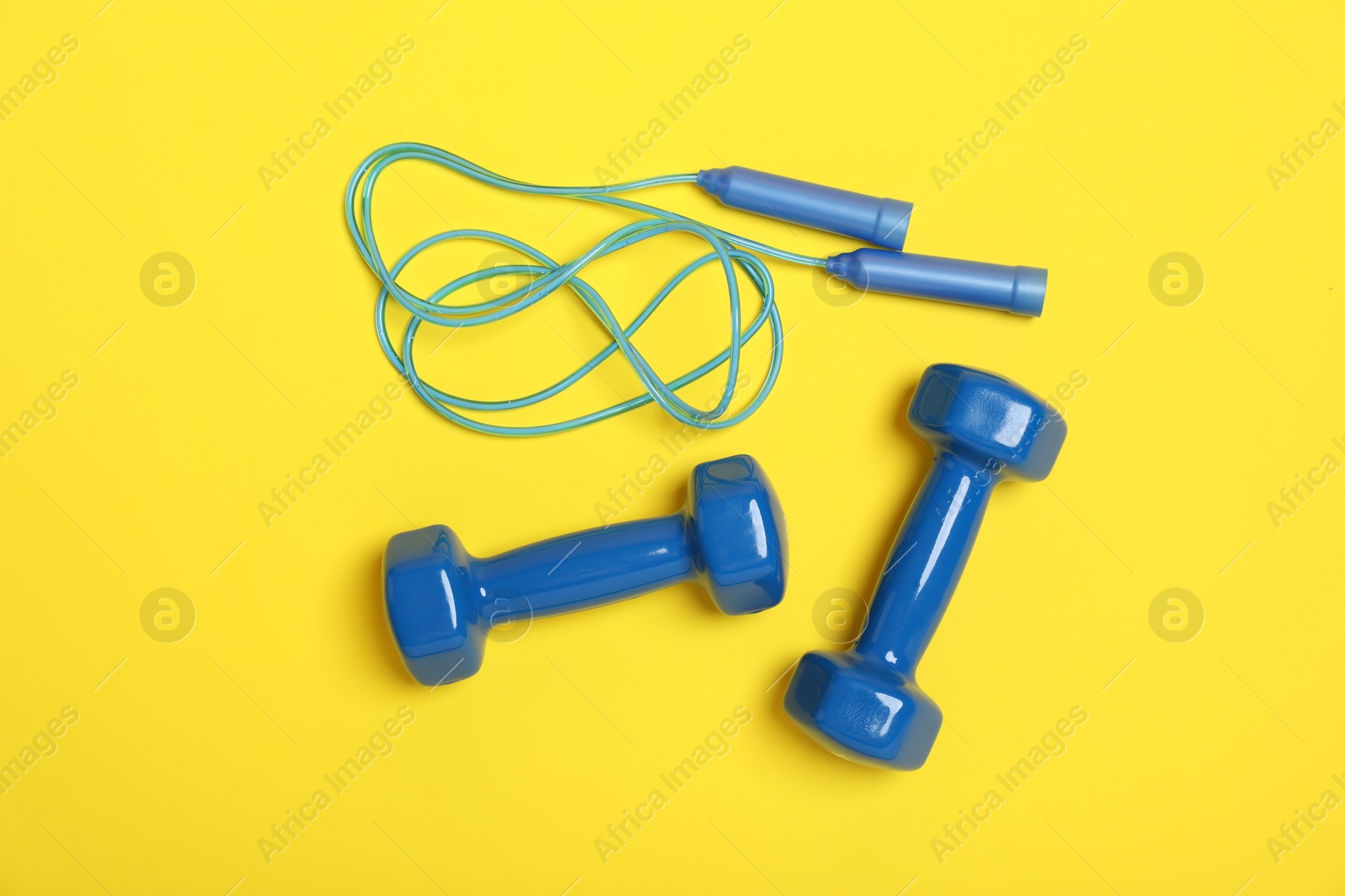 Photo of Skipping rope and dumbbells on yellow background, flat lay. Sports equipment