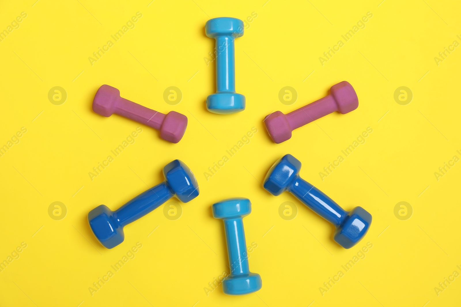 Photo of Different dumbbells on yellow background, flat lay. Sports equipment