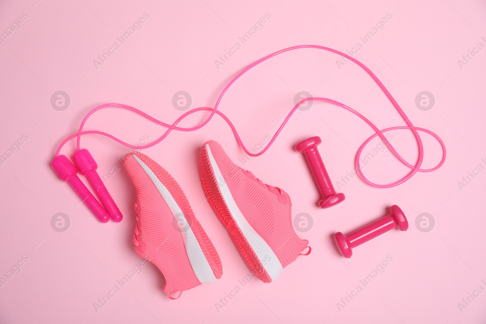 Photo of Skipping rope, sneakers and dumbbells on pink background, flat lay. Sports equipment