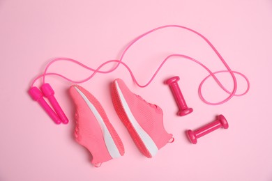 Photo of Skipping rope, sneakers and dumbbells on pink background, flat lay. Sports equipment