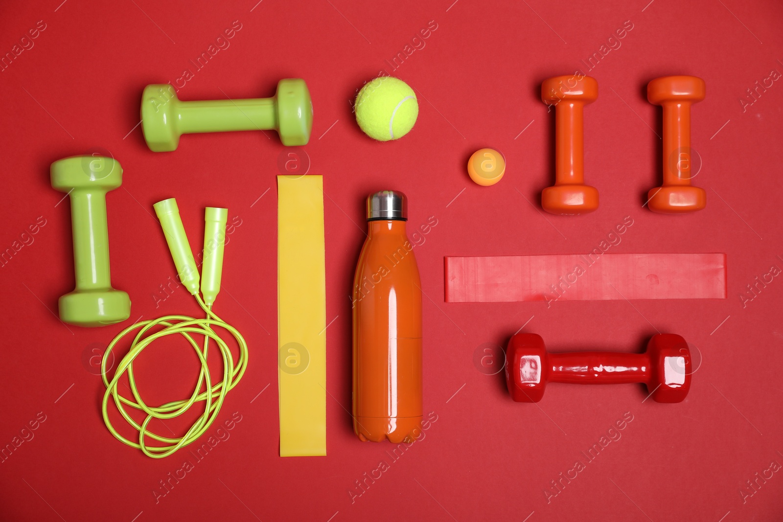 Photo of Different sports equipment and water bottle on red background, flat lay