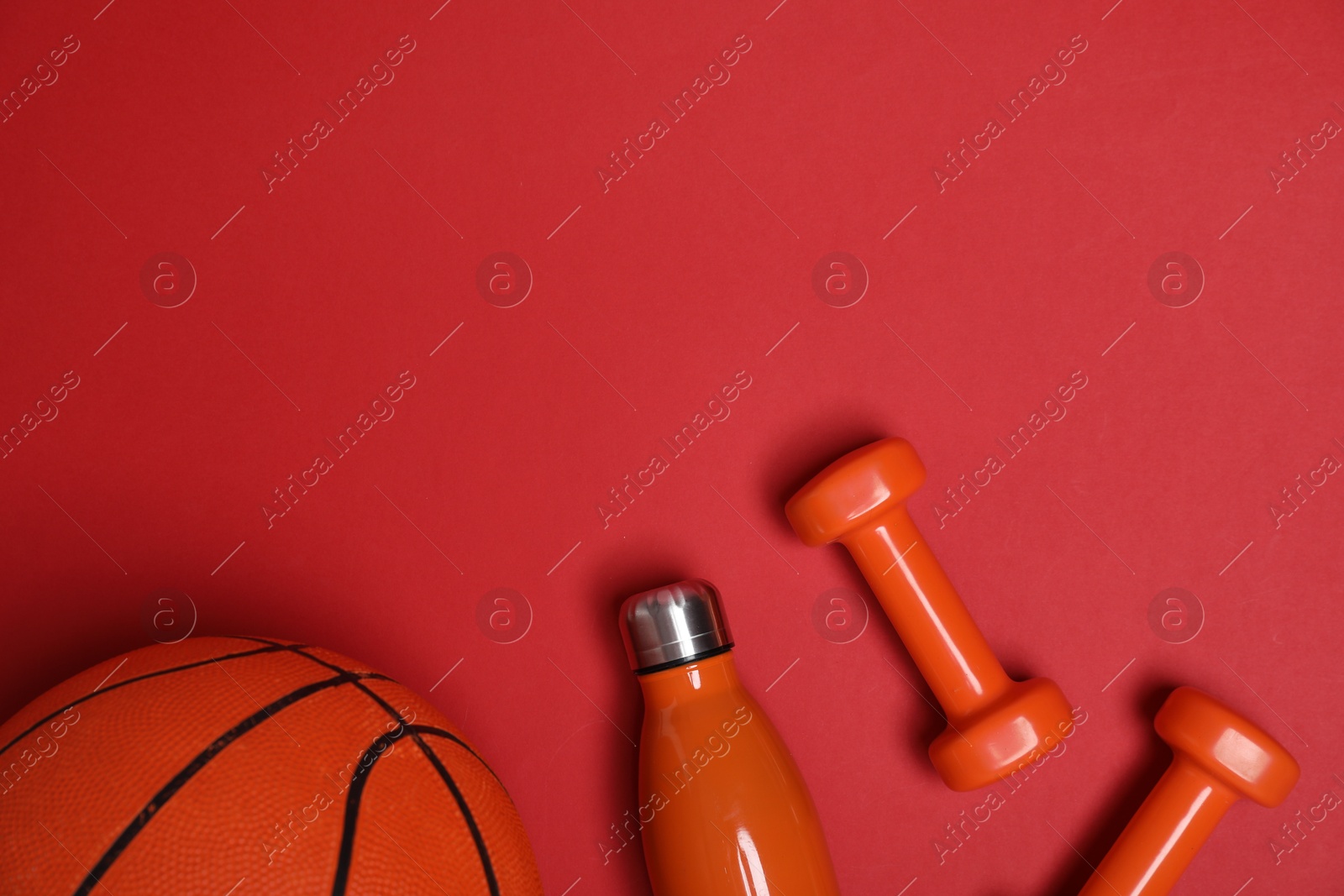 Photo of Sports equipment. Dumbbells, water bottle and basketball ball on red background, flat lay. Space for text