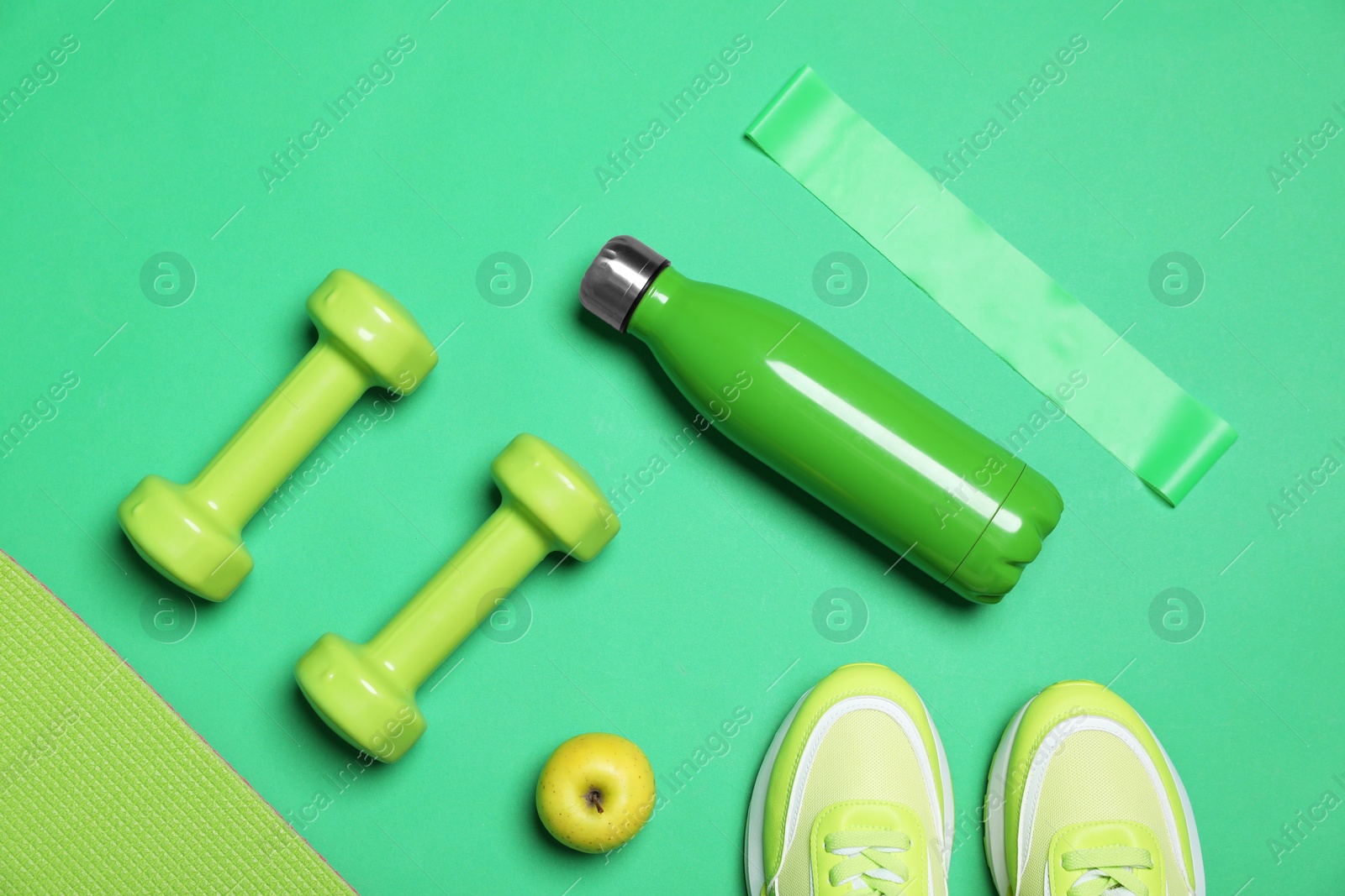 Photo of Different sports equipment, apple and sneakers on green background, flat lay