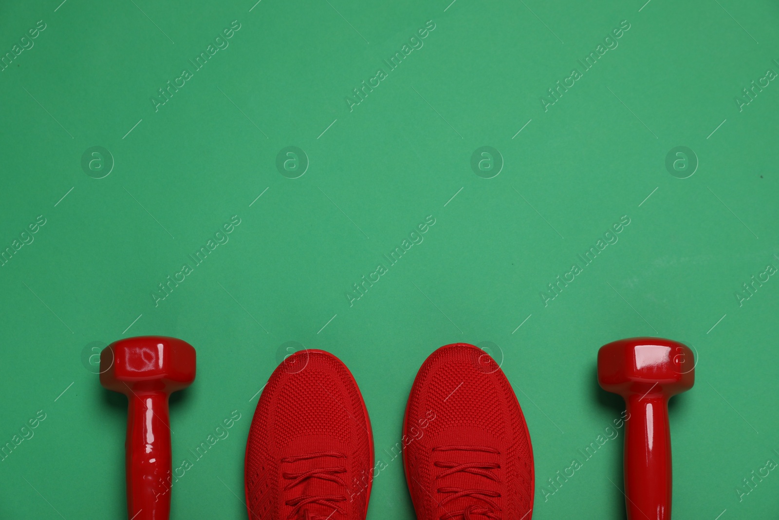 Photo of Sports equipment. Dumbbells and sneakers on green background, flat lay. Space for text