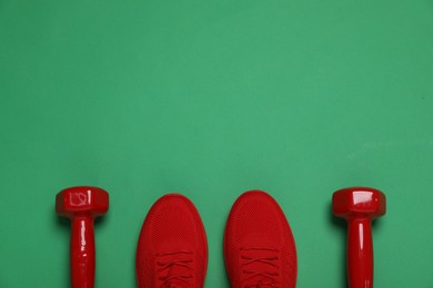 Photo of Sports equipment. Dumbbells and sneakers on green background, flat lay. Space for text