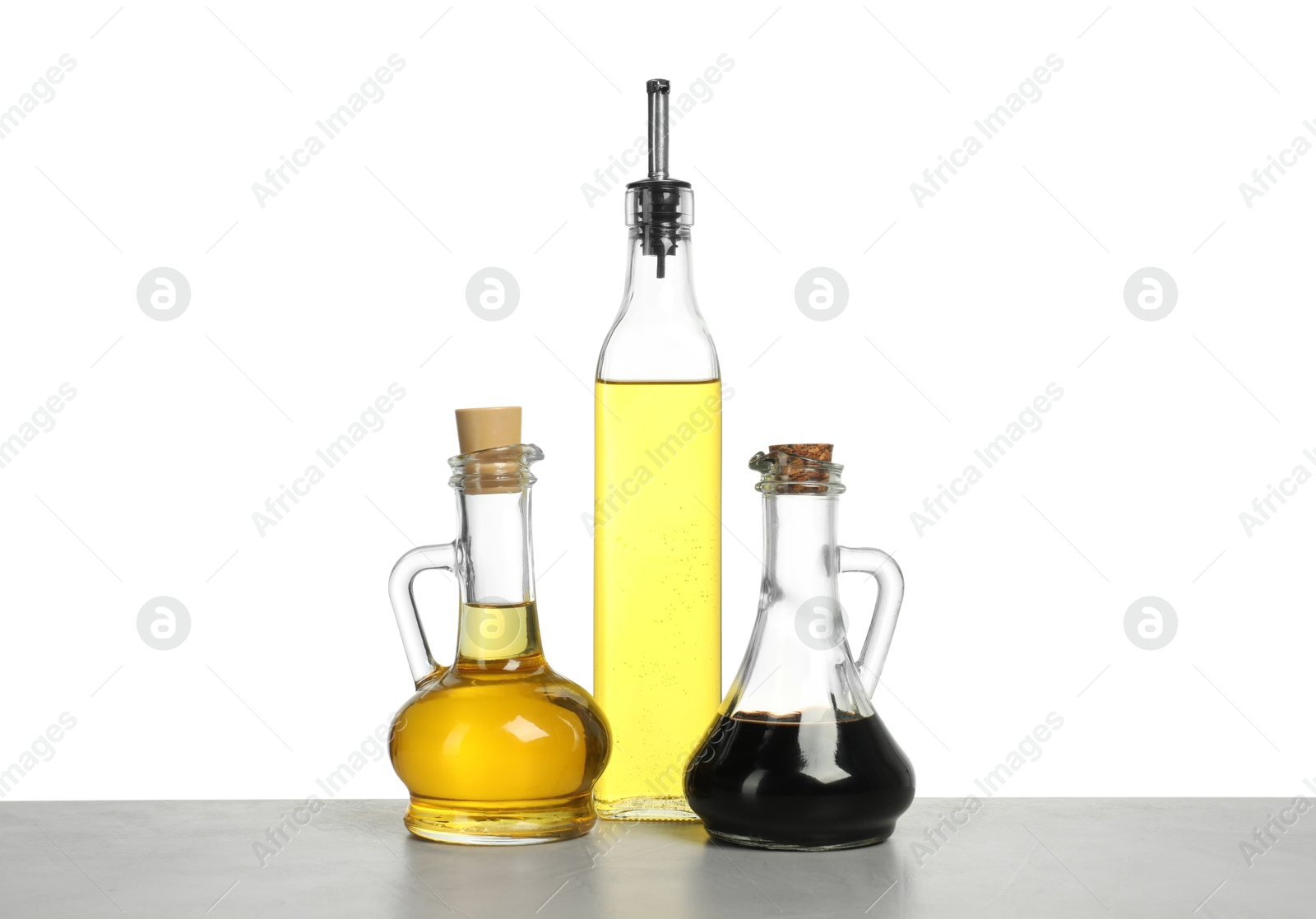 Photo of Oils and vinegar in bottles on table against white background