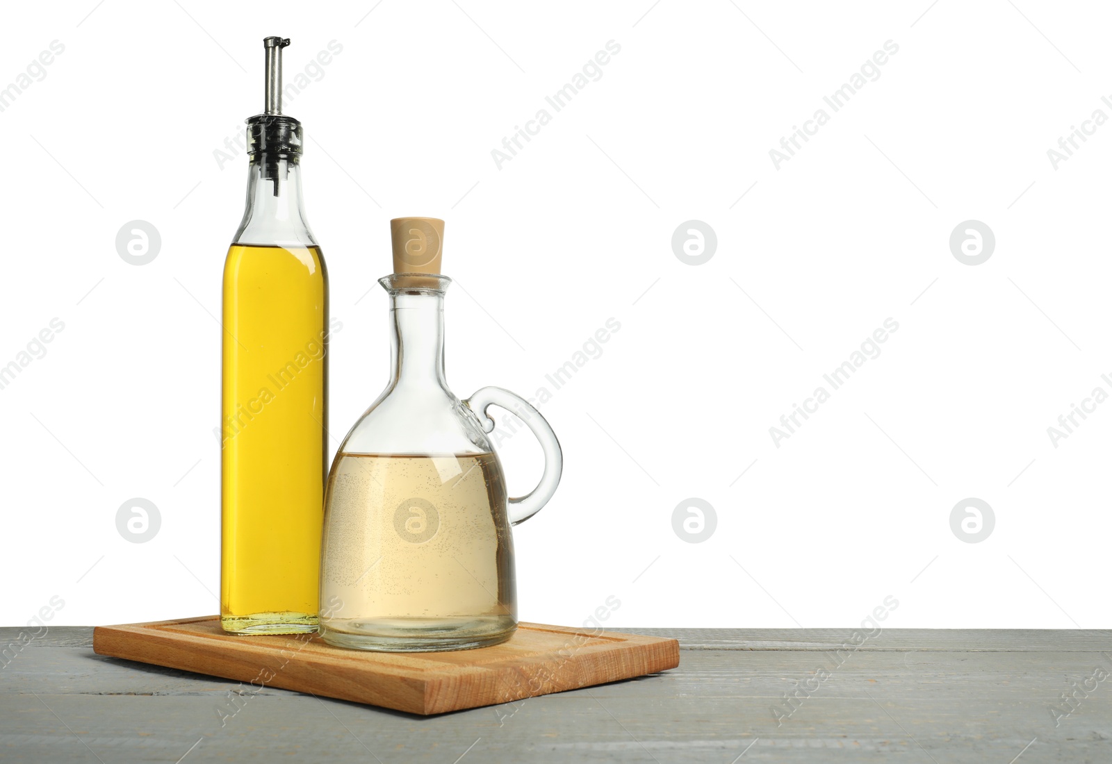 Photo of Oil and vinegar in bottles on grey wooden table against white background