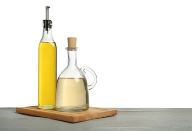 Photo of Oil and vinegar in bottles on grey wooden table against white background