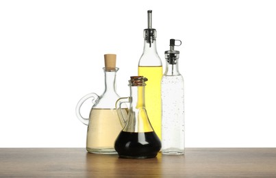 Photo of Oil and vinegars in bottles on wooden table against white background