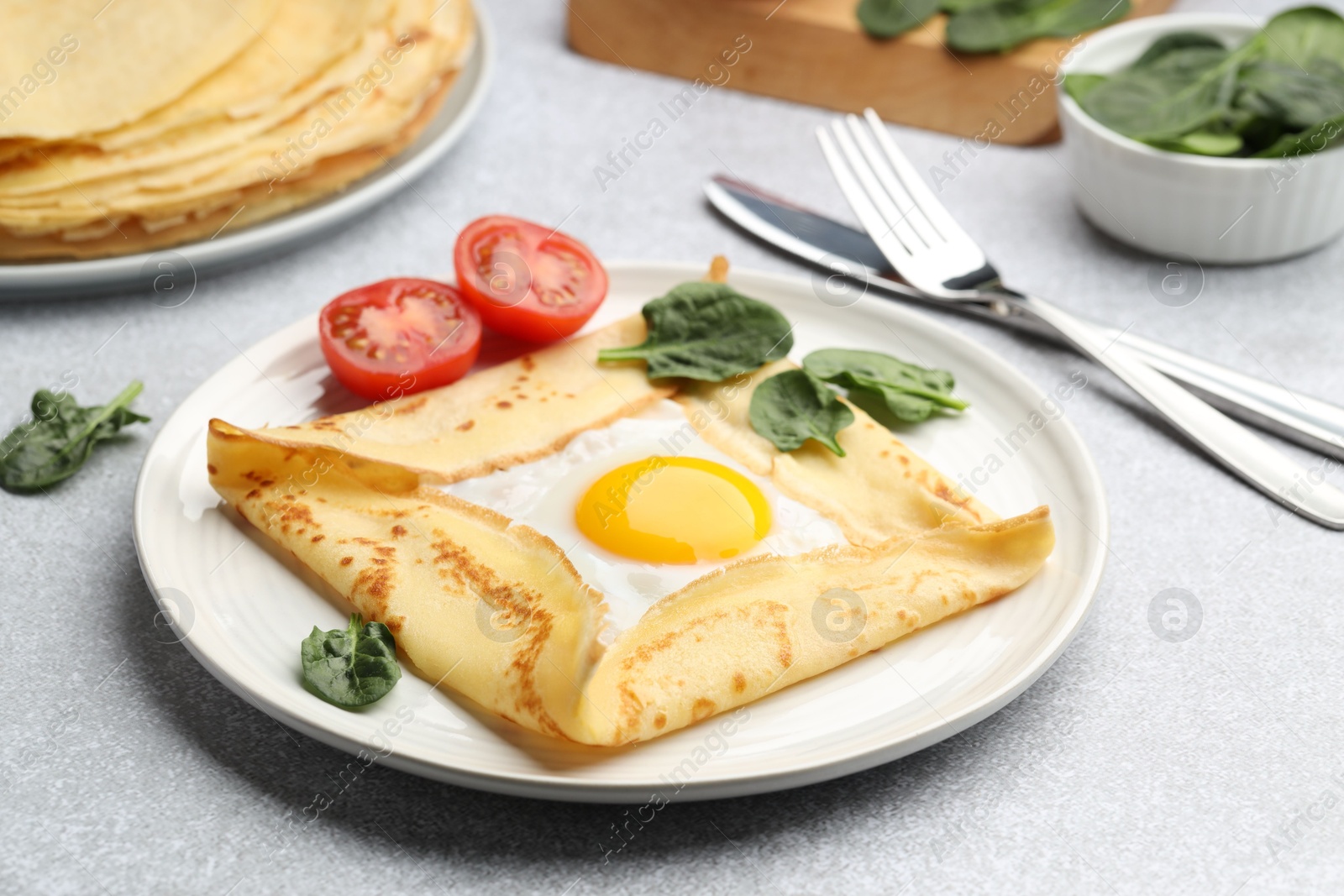 Photo of Delicious crepe with egg, tomato and basil on light grey table, closeup