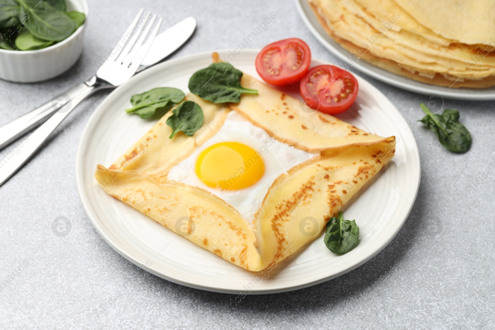 Photo of Delicious crepe with egg, tomato and basil on light grey table, closeup