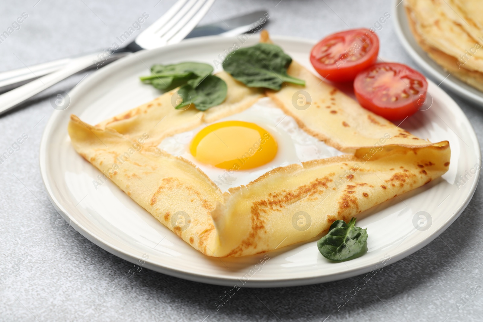 Photo of Delicious crepe with egg, tomato and basil on light grey table, closeup