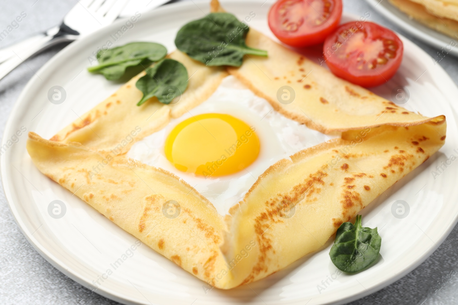 Photo of Delicious crepe with egg, tomato and basil on table, closeup