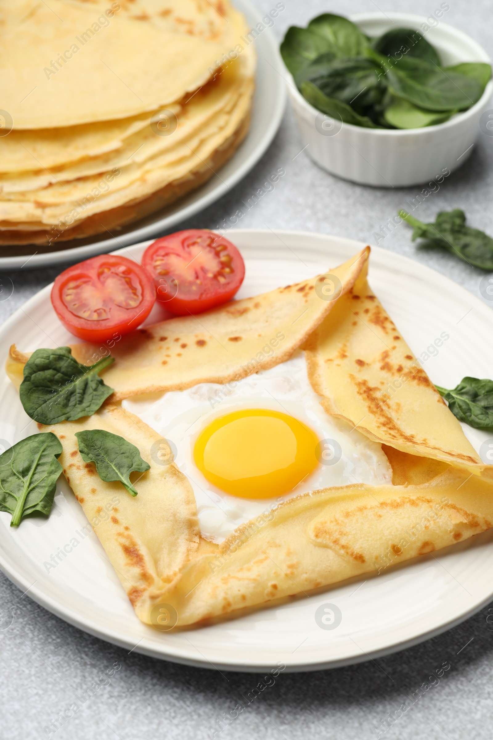 Photo of Delicious crepes with egg, tomato and basil on light grey table, closeup