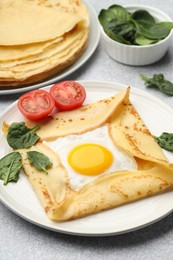 Photo of Delicious crepes with egg, tomato and basil on light grey table, closeup