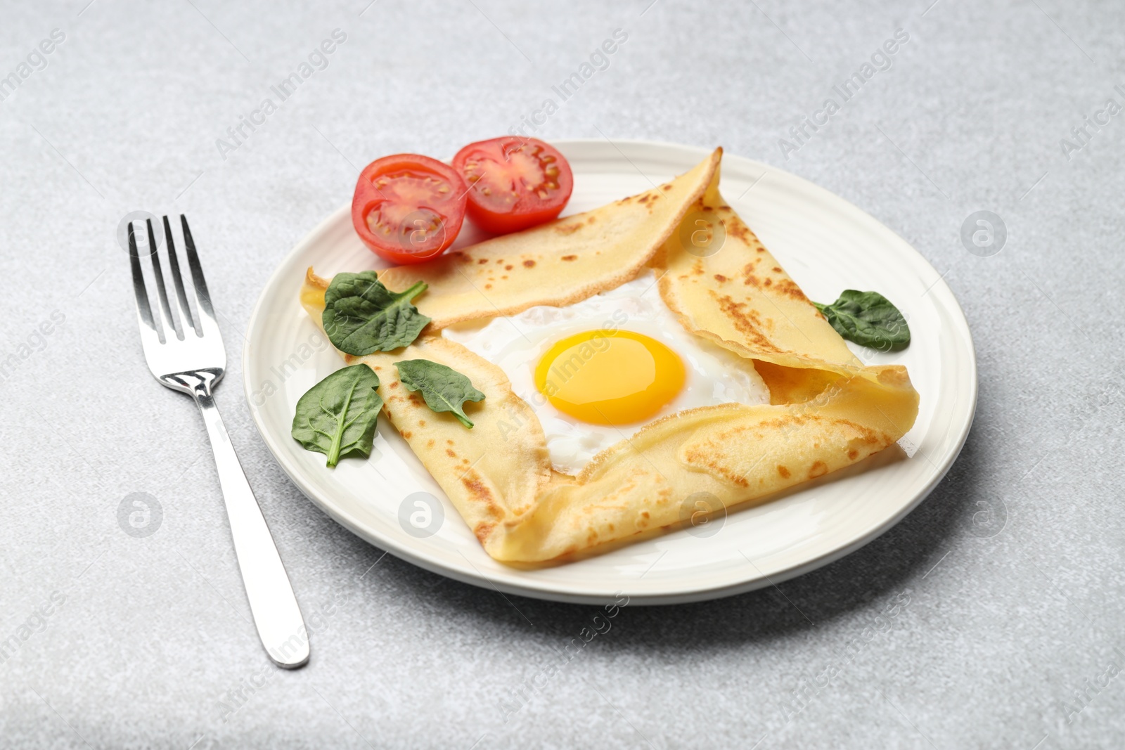 Photo of Delicious crepe with egg, tomato and basil on light grey table, closeup