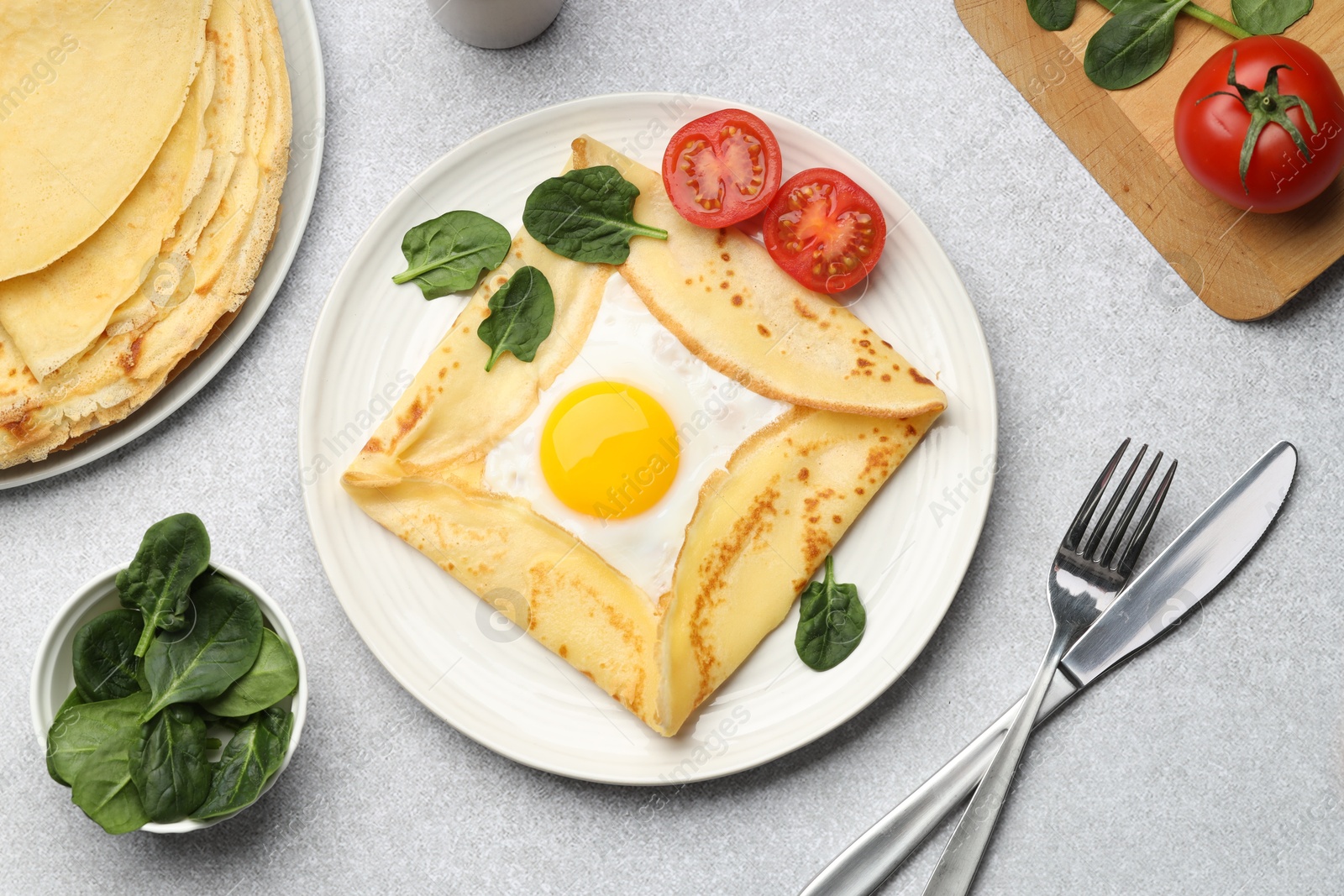 Photo of Delicious crepes with egg, tomatoes and basil on light grey table, flat lay