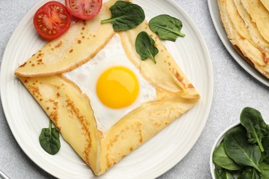 Photo of Delicious crepes with egg, tomato and basil on light grey table, flat lay