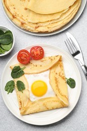 Photo of Delicious crepes with egg, tomato and basil on light grey table, flat lay