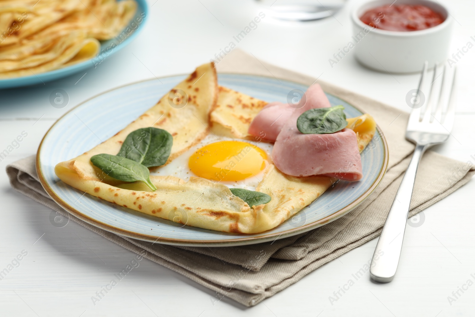 Photo of Delicious crepe with egg, ham and basil on white wooden table, closeup