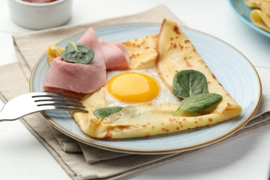 Photo of Delicious crepe with egg, ham and basil on white wooden table, closeup