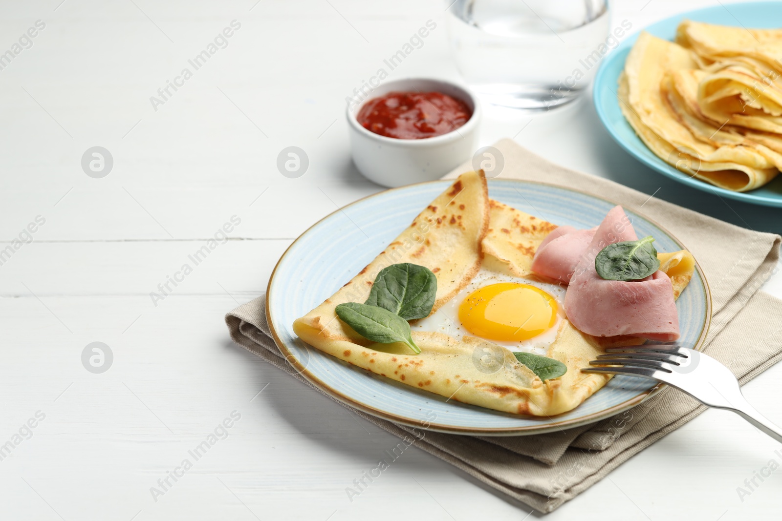 Photo of Delicious crepes with egg, ham, basil and sauce on white wooden table, closeup. Space for text